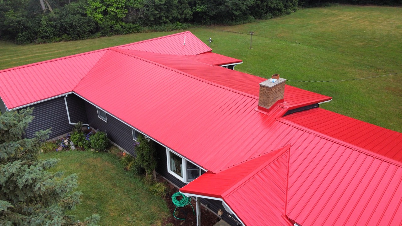 Aerial view of a completed red standing-seam metal roof with several roof planes and a chimney