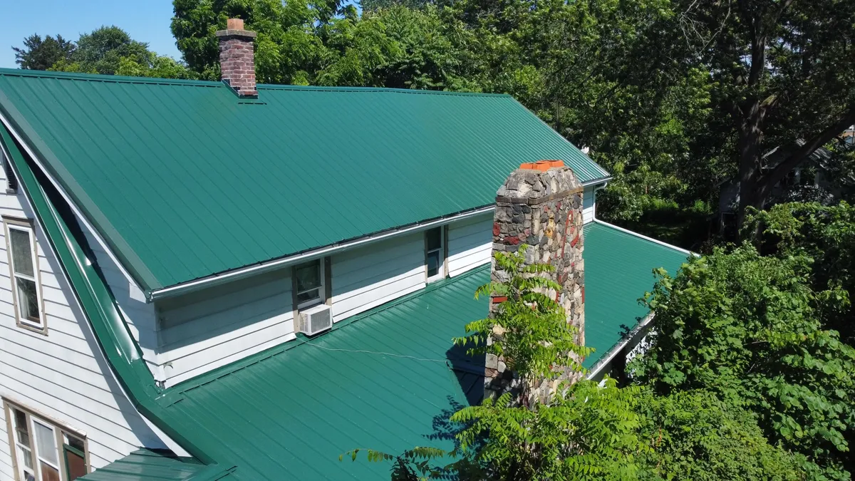 Aerial view of green standing seam metal roof on historic home with stone chimney