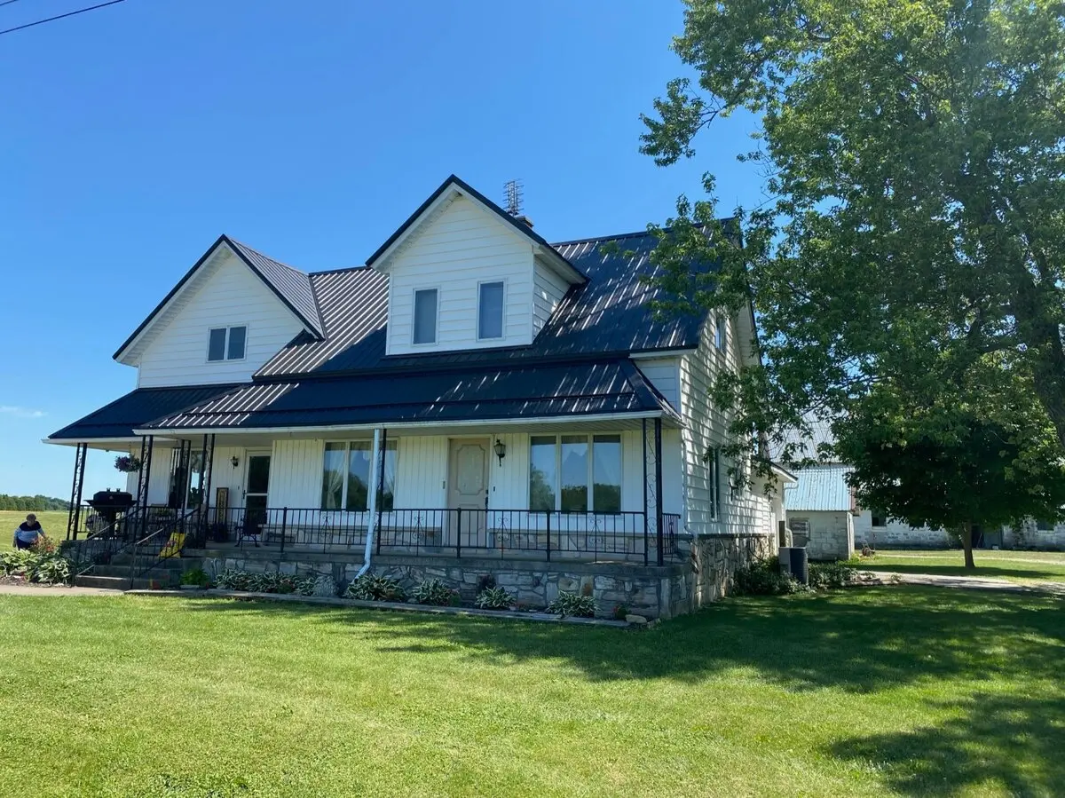 Black standing seam metal roof on classic farmhouse with wrap-around porch